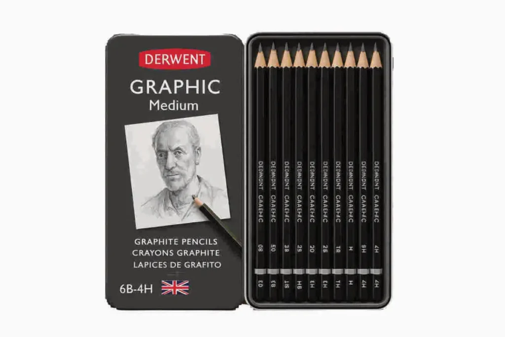 Derwent Graphic Medium pencil set in gray metal tin with 12 graphite pencils from 6B to 4H, lid showing portrait sketch and UK flag, placed on wooden surface