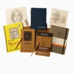 Top 5 drawing paper pads including Strathmore, Canson, Arteza, Fabriano, and Moleskine arranged on wood surface with sketches and pencils around them.