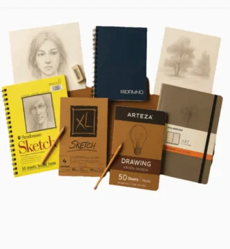 Top 5 drawing paper pads including Strathmore, Canson, Arteza, Fabriano, and Moleskine arranged on wood surface with sketches and pencils around them.