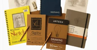 Top 5 drawing paper pads including Strathmore, Canson, Arteza, Fabriano, and Moleskine arranged on wood surface with sketches and pencils around them.