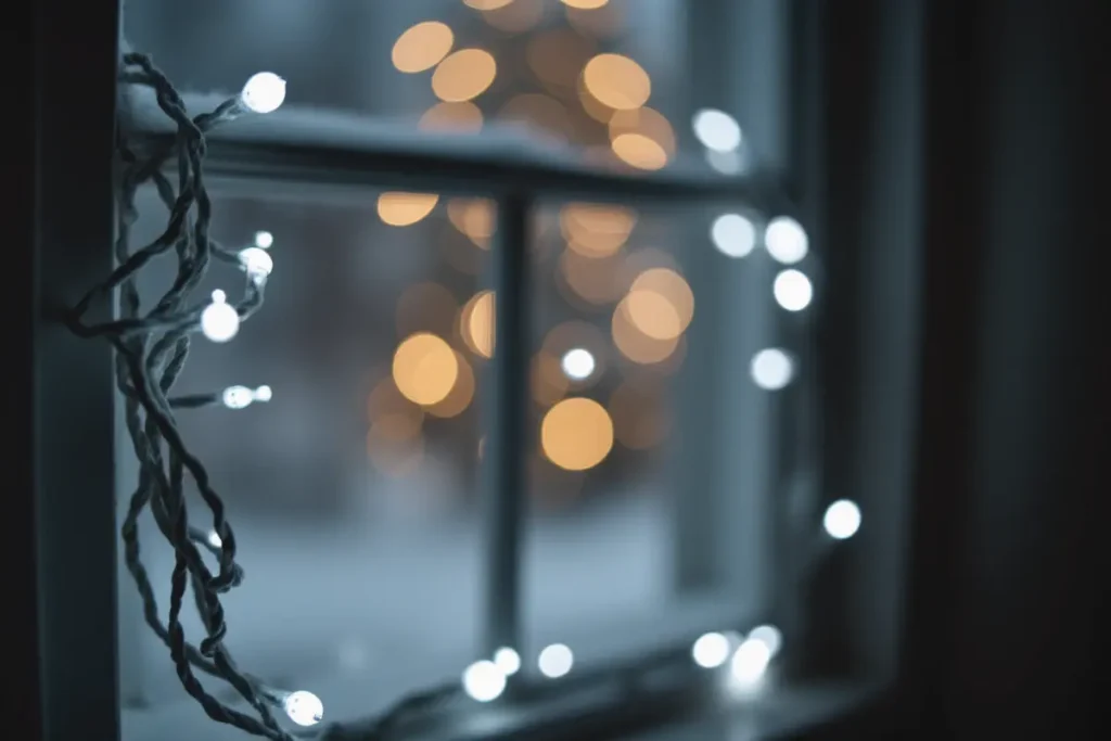 Detalle de luces LED blancas colgadas en el marco de una ventana navideña.”